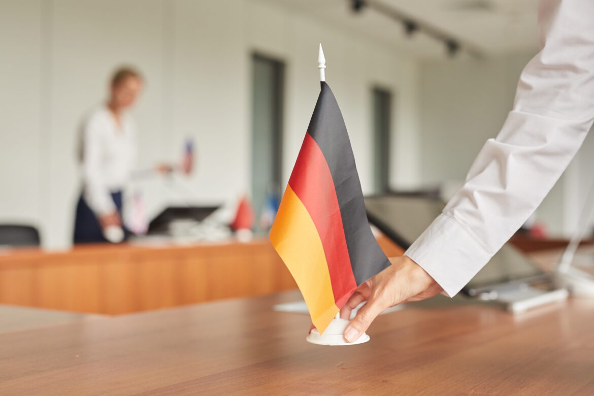 nahaufnahme-der-weiblichen-assistentin-die-deutsche-flagge-auf-tisch-setzt-wahrend-konferenzraum-fur-internationales-geschaftsereignis-vorbereitet Kopie